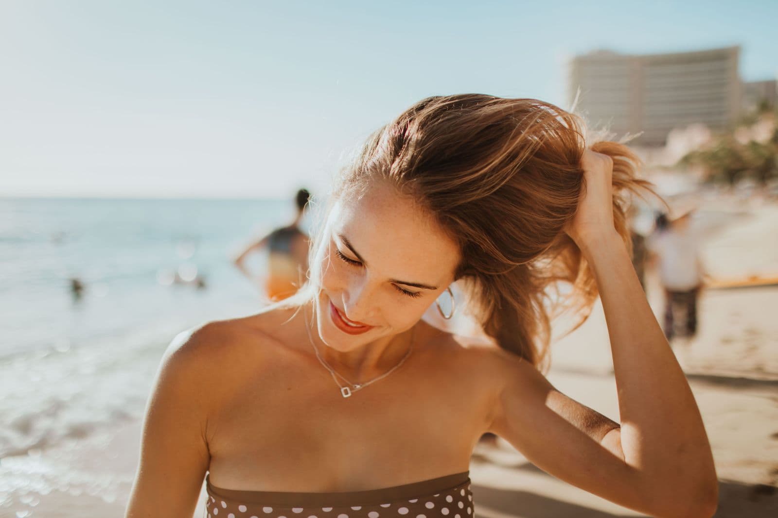 A woman tying back sun-lit hair on the beach on a summer holiday